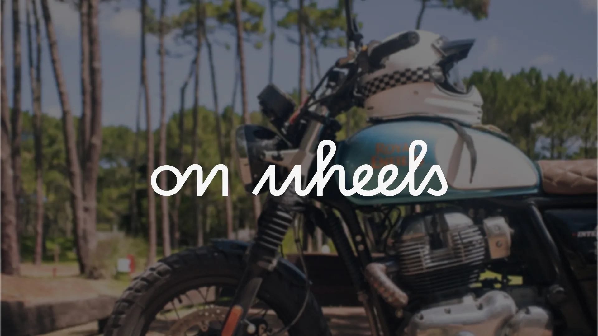 Logo blanc On Wheels appliquée sur une photo de moto en extérieur.